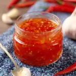 Homemade Chili Garlic Sauce in a glass jar with chili peppers and garlic